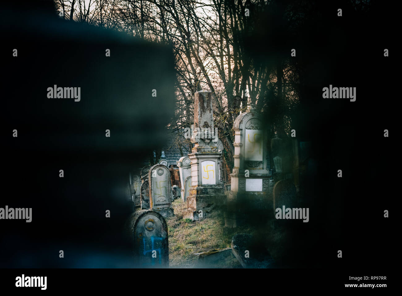 Vista attraverso le pietre del soggetto ad atti vandalici tombe con simboli nazisti in giallo spray-dipinte sulle tombe danneggiato - Cimitero Ebraico in Quatzenheim vicino a Strasbourg, Francia Foto Stock