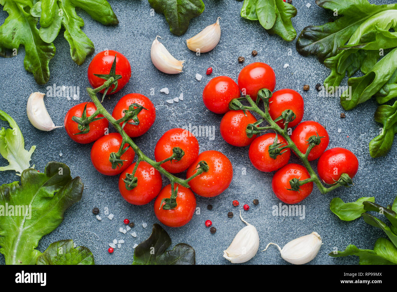 Pomodori ciliegia su un ramo di erbe fresche e uno spicchio di aglio con spezie al buio su un tavolo di pietra Foto Stock