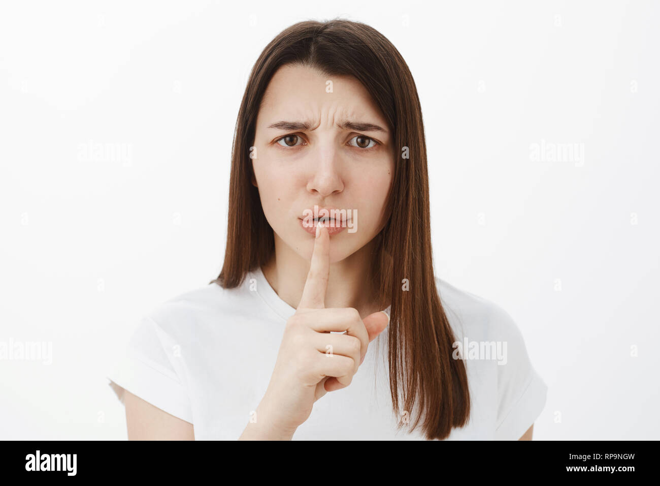 La shh è promessa soggiorno tranquillo. Ritratto di orinato e sconvolto carino brunette in 20s accigliata deluso tenendo il dito indice sulla bocca come per chiedere di mantenere Foto Stock