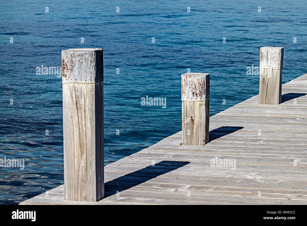 Un piccolo molo e la sua piazza tre poli di ormeggio che creare giochi geometrici con le ombre e la simmetria delle tavole di legno della banchina sul Foto Stock