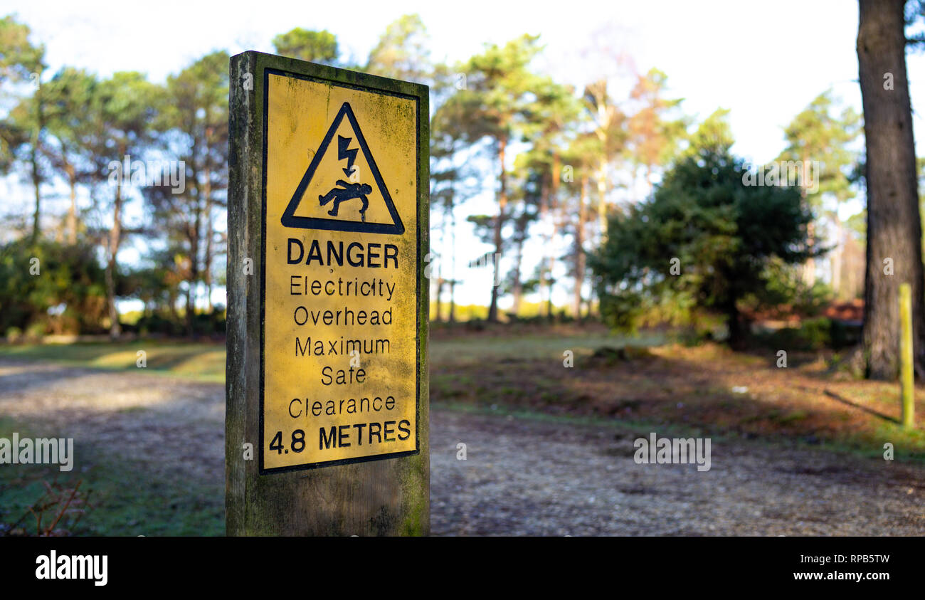 Segnale di avvertimento evidenziando il pericolo di sovraccarico linee elettriche al di sopra di passeggiate e percorsi in bicicletta a New Forest Hampshire Inghilterra. Foto Stock