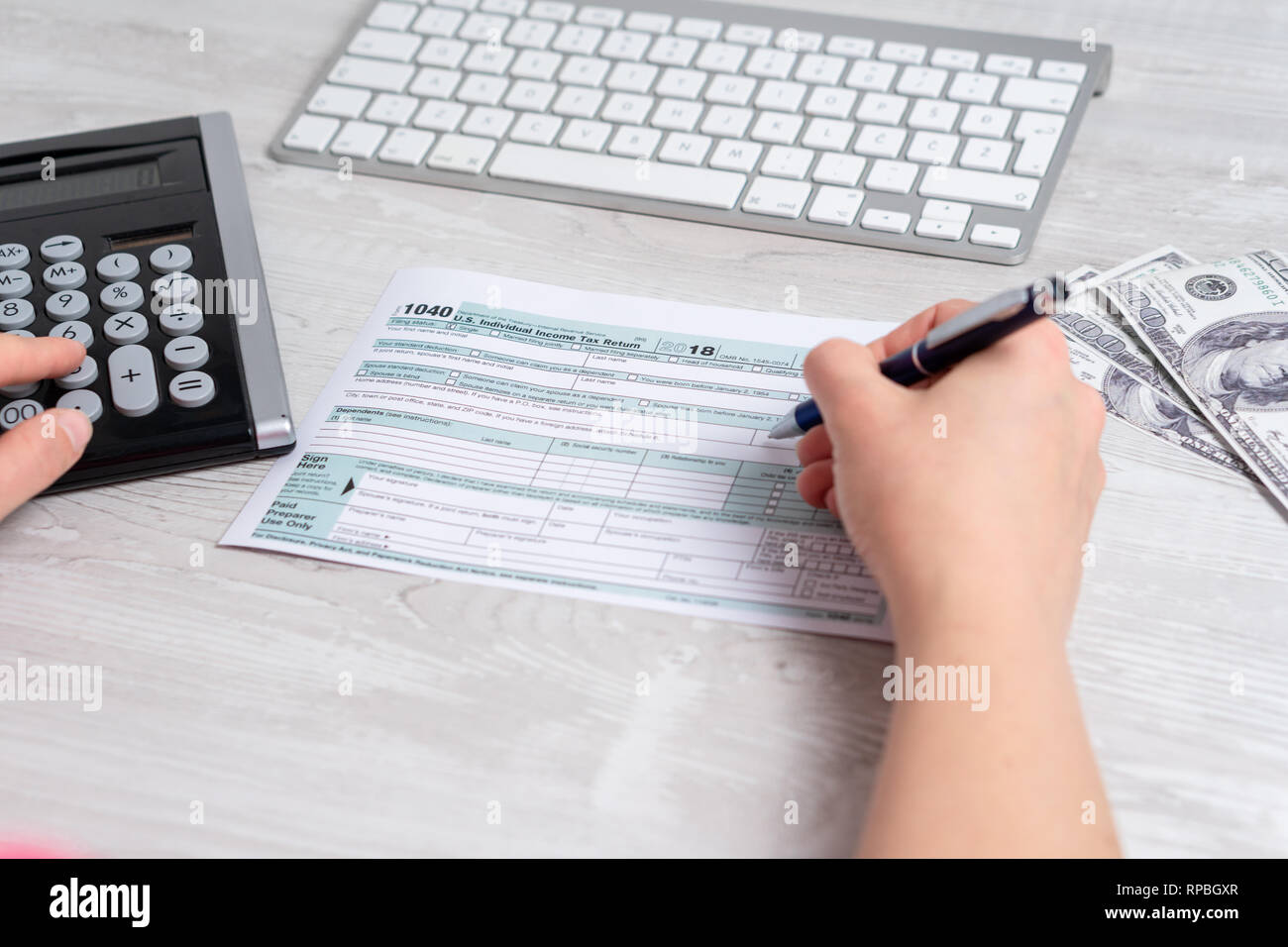 Punto di vista foto di donna e di calcolo e il riempimento di noi sotto forma di imposta accanto alla tastiera del computer, le fatture del dollaro e forma fiscale 1040. 15 aprile 2019 giornata fiscale Foto Stock