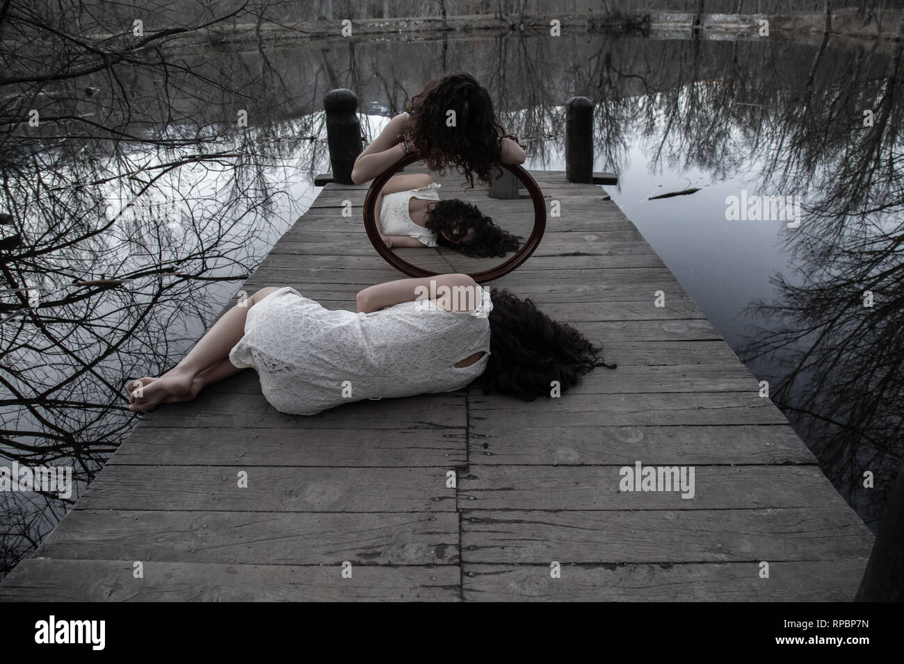 Irriconoscibile gemelli nella stessa bianco vestiti in posa con specchio sul molo in legno al lago calmo sui giorni di autunno Foto Stock
