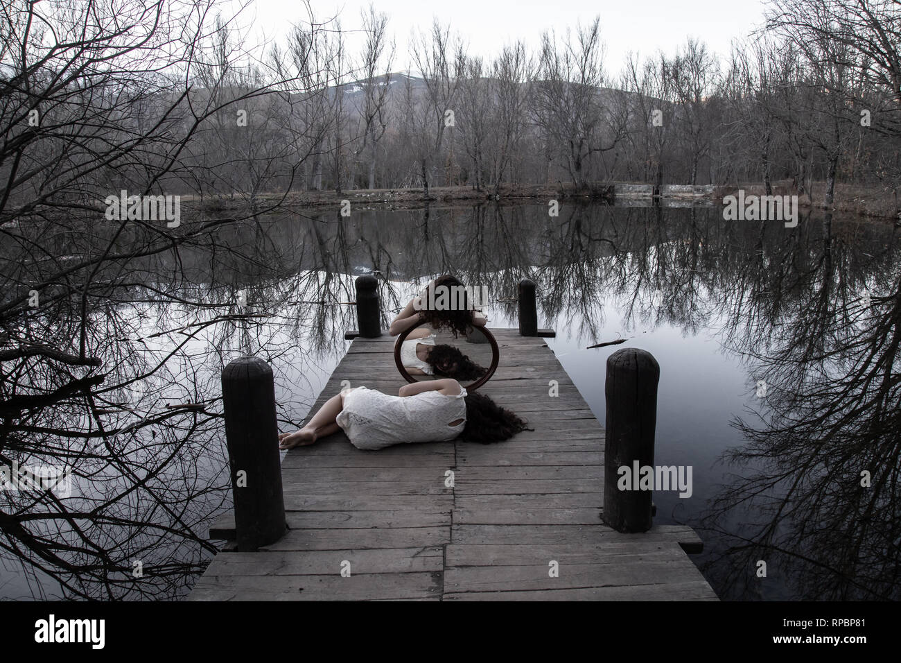 Irriconoscibile gemelli nella stessa bianco vestiti in posa con specchio sul molo in legno al lago calmo sui giorni di autunno Foto Stock