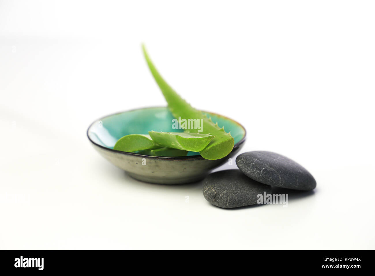 l'aloe vera si allena in una piccola ciotola, con pietre termali su sfondo bianco Foto Stock