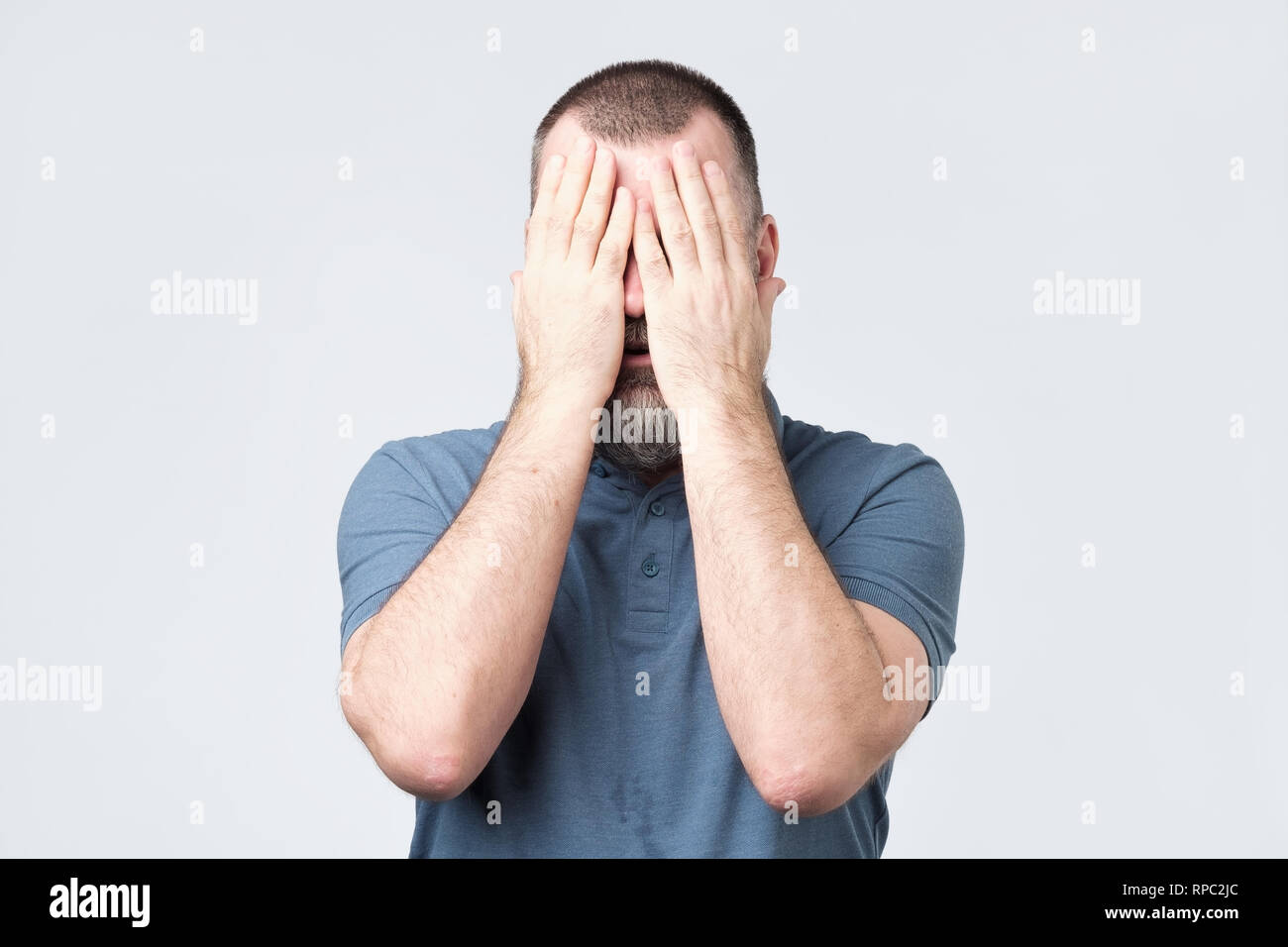 Uomo in maglietta blu che copre il volto con le mani Foto Stock