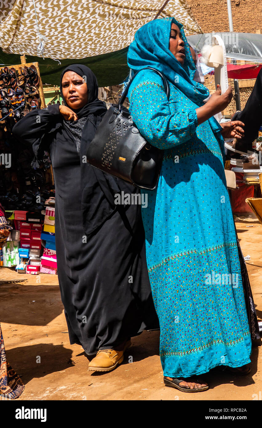 Il governo di Khartoum, Sudan, 5 febbraio. 2019: due donne con lunghi vestiti e il velo al mercato, una donna in blu Abaya negoziando l'acquisto di bianco Foto Stock