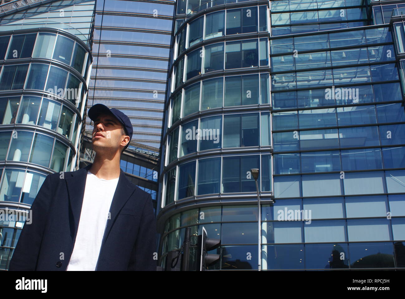 Giovane maschio normale turista con tappo a esplorare una città moderna con finestra di vetro edificio in background Foto Stock