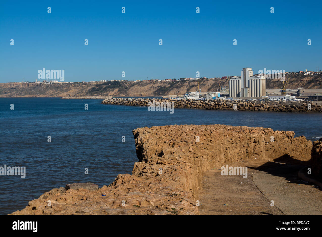 Costa dell'Oceano Atlantico. Azzurro cielo. Percorso con un rivestimento in pietra. La fabbrica in background. Safi, Marocco. Foto Stock