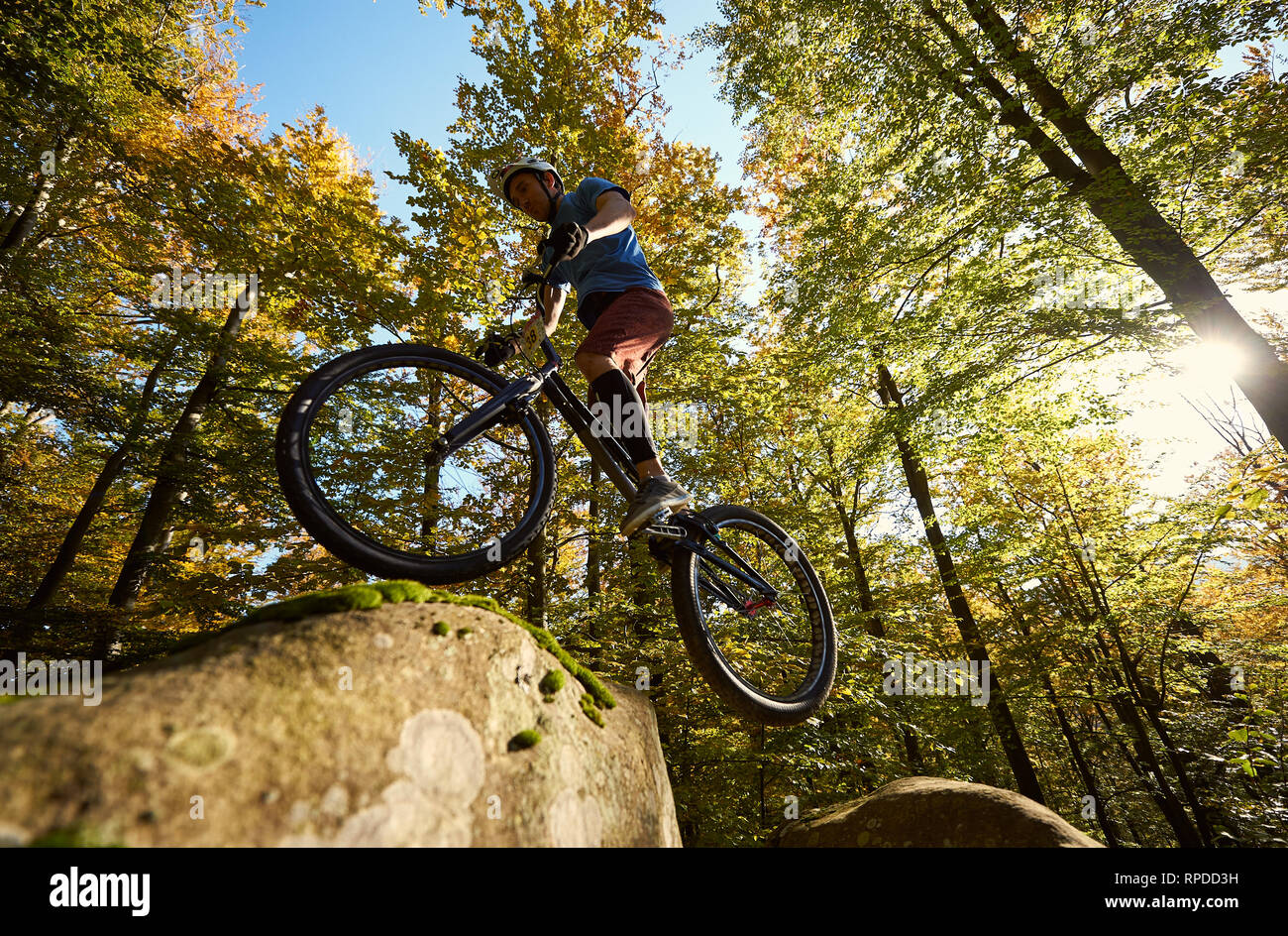 Ciclista professionista salto sulla bicicletta di prova sul grosso masso. Basso angolo di visione del pilota maschio rendendo trucco acrobatico nella foresta in estate giornata di sole. Concetto di sport estremo che uno stile di vita attivo Foto Stock