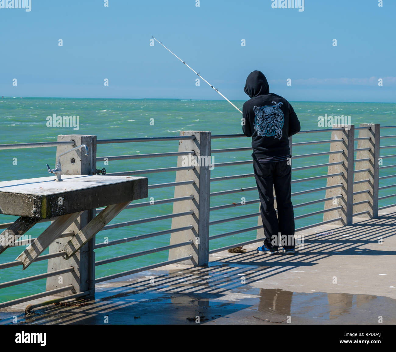 Un uomo che indossa una felpa con cappuccio nero è la pesca al largo di un molo di Fort De Soto park in Florida Foto Stock