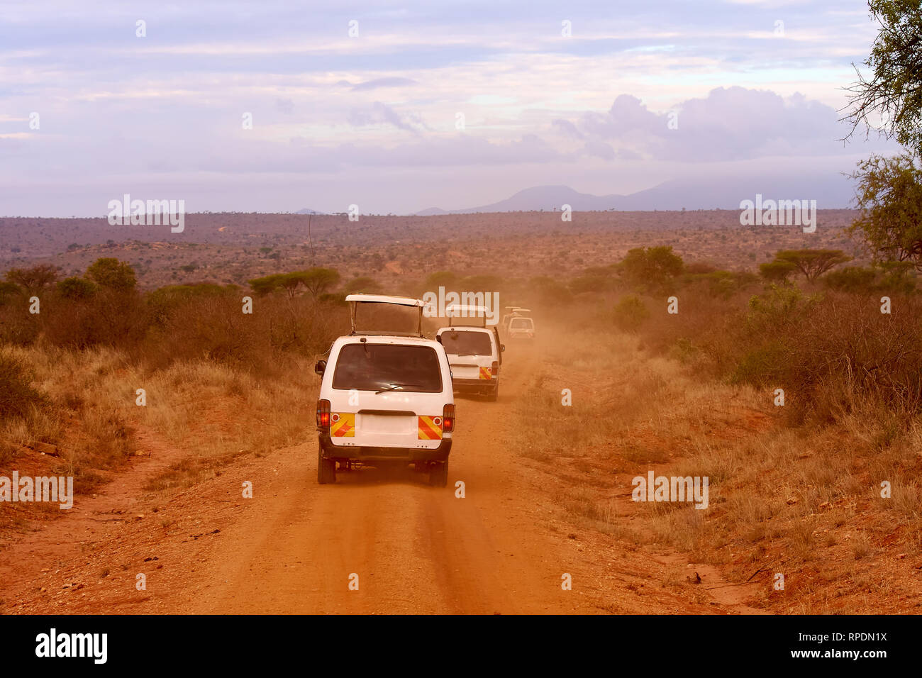 Numerose vetture di safari in Kenya in Africa, sabbia rossa e montagne sullo sfondo Foto Stock