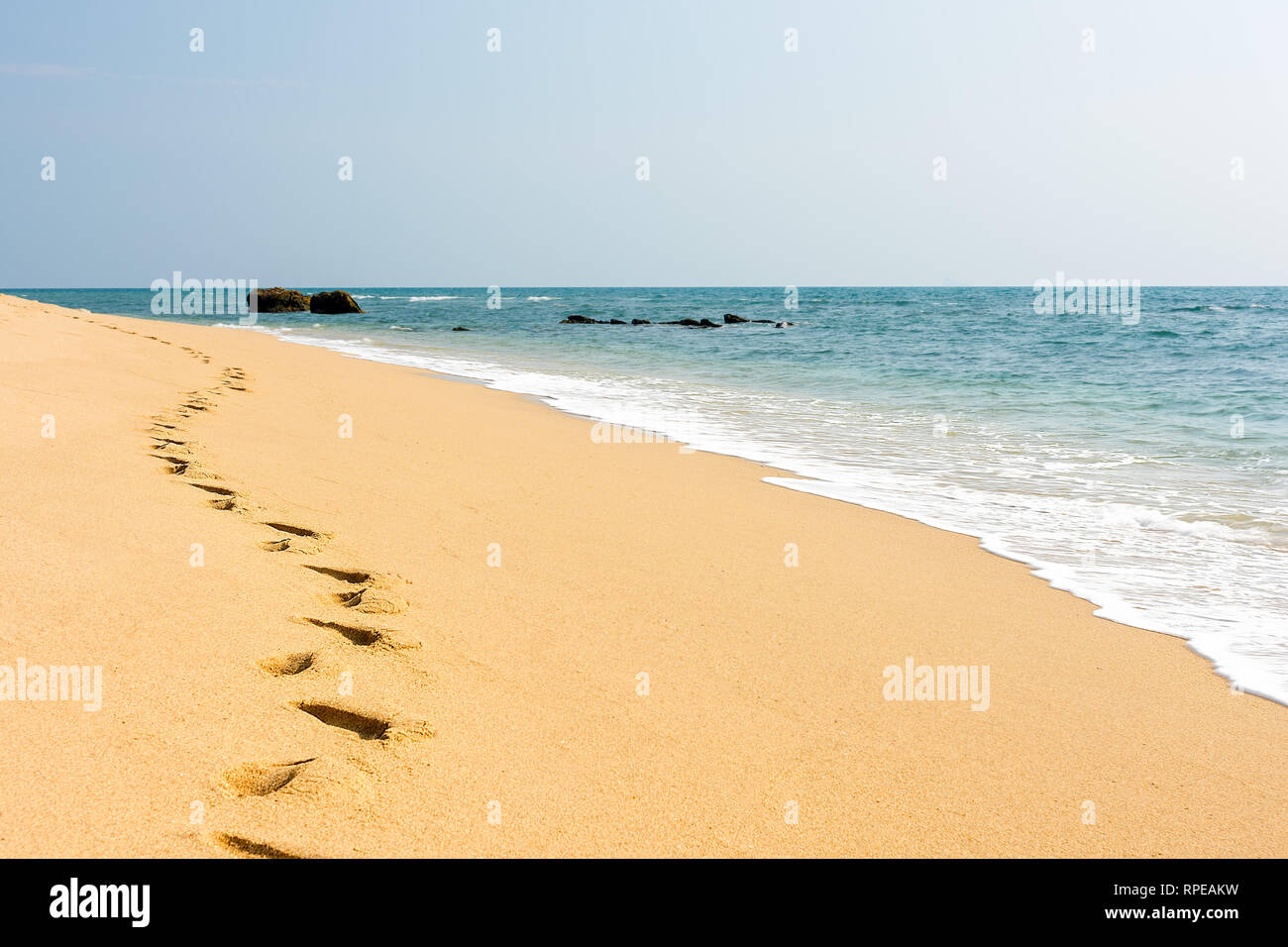 Piedi di stampe in un chiaro sabbia dorata spiaggia perfetta accanto a una calma il mare turchese. Foto Stock