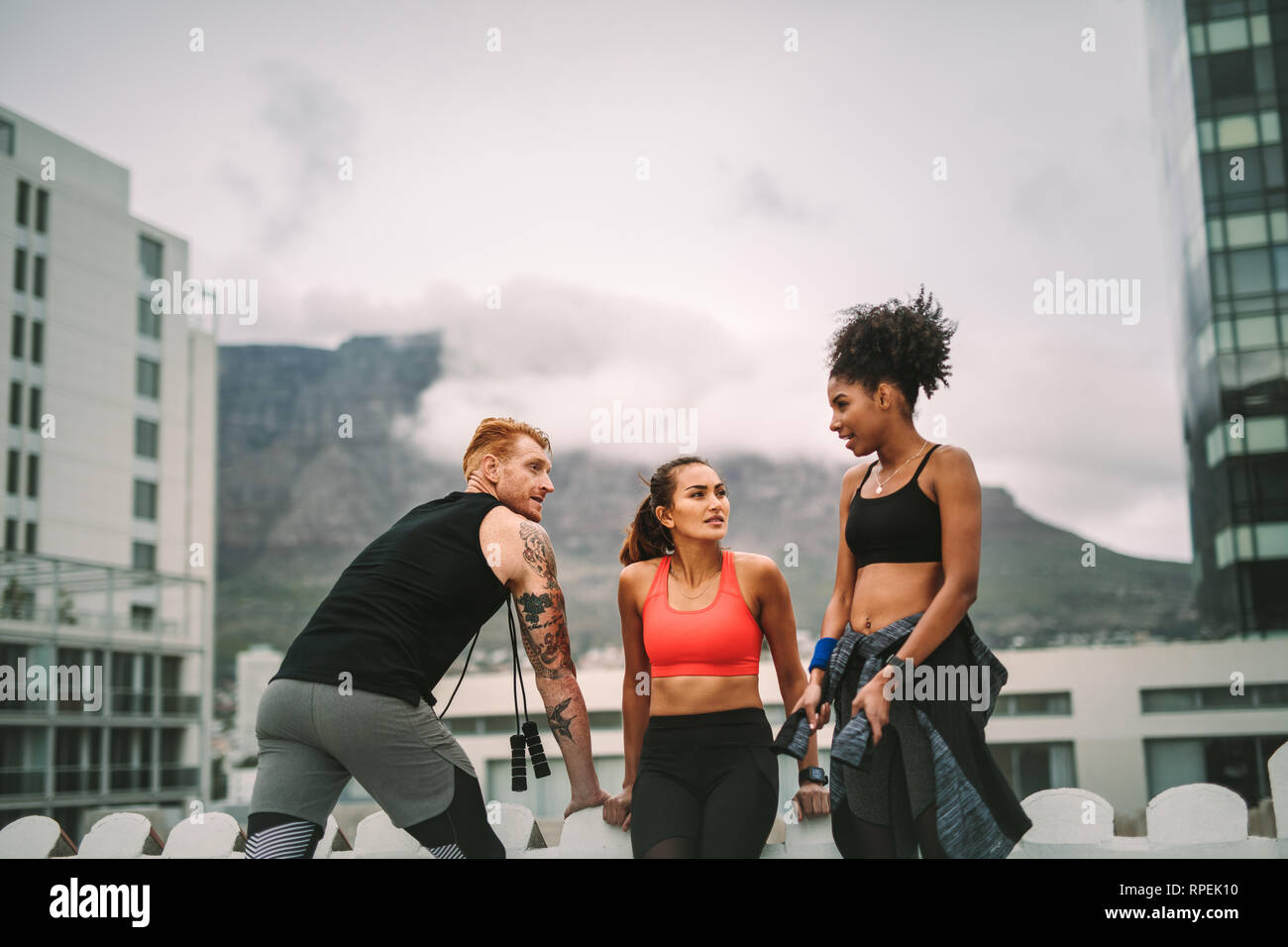 Due donne del fitness con un uomo che si rilassa dopo l'allenamento sul tetto e parla tra loro. fitness in piedi sulla terrazza dopo l'allenamento Foto Stock