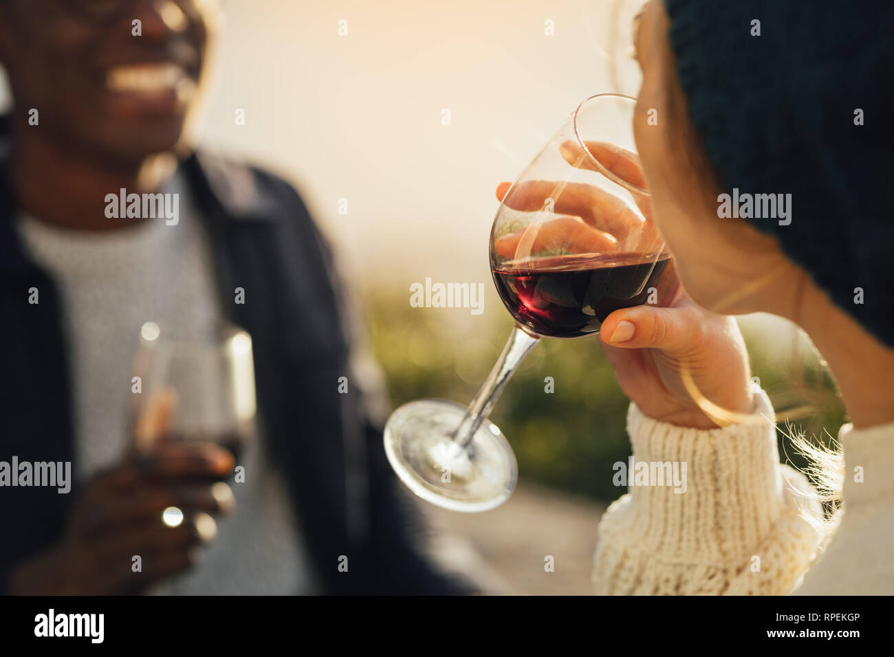 Close-up di donna bere il vino con il suo ragazzo seduto sul retro. Coppia avente un picnic con focus sul bicchiere di vino in mano della femmina. Foto Stock