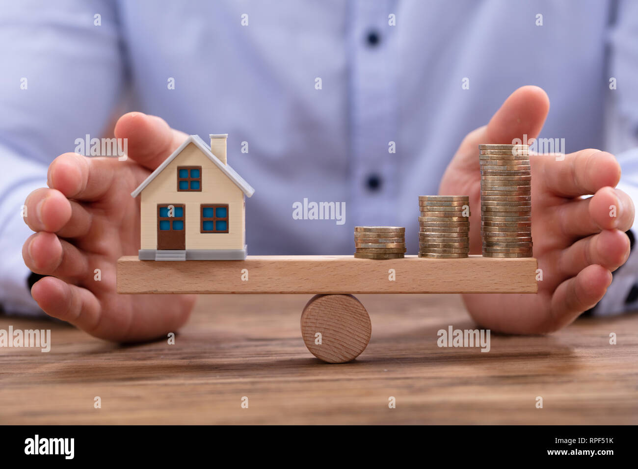 Piccola casa modello e impilati monete d oro in equilibrio su altalena in legno Foto Stock