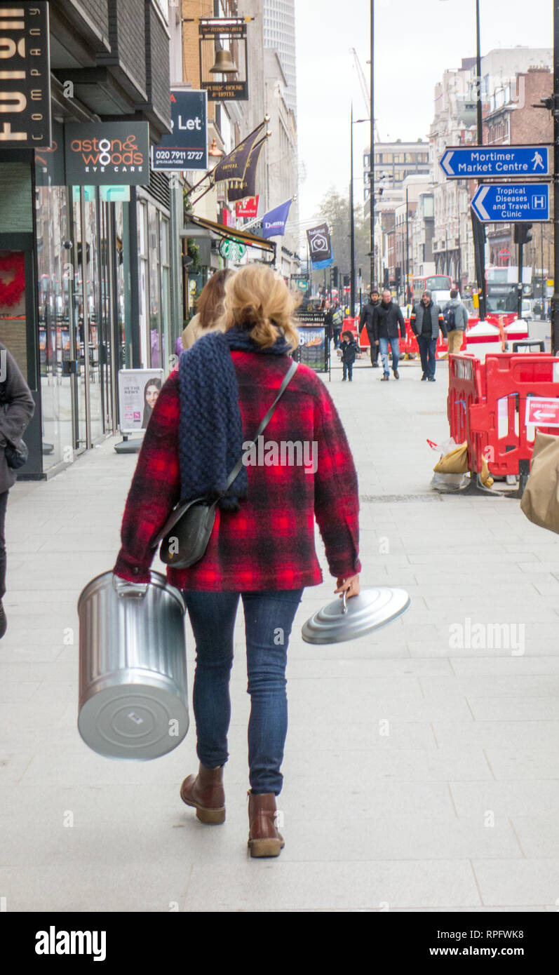 La donna a piedi attraverso il centro di Londra che porta un bidone della spazzatura e del coperchio Foto Stock