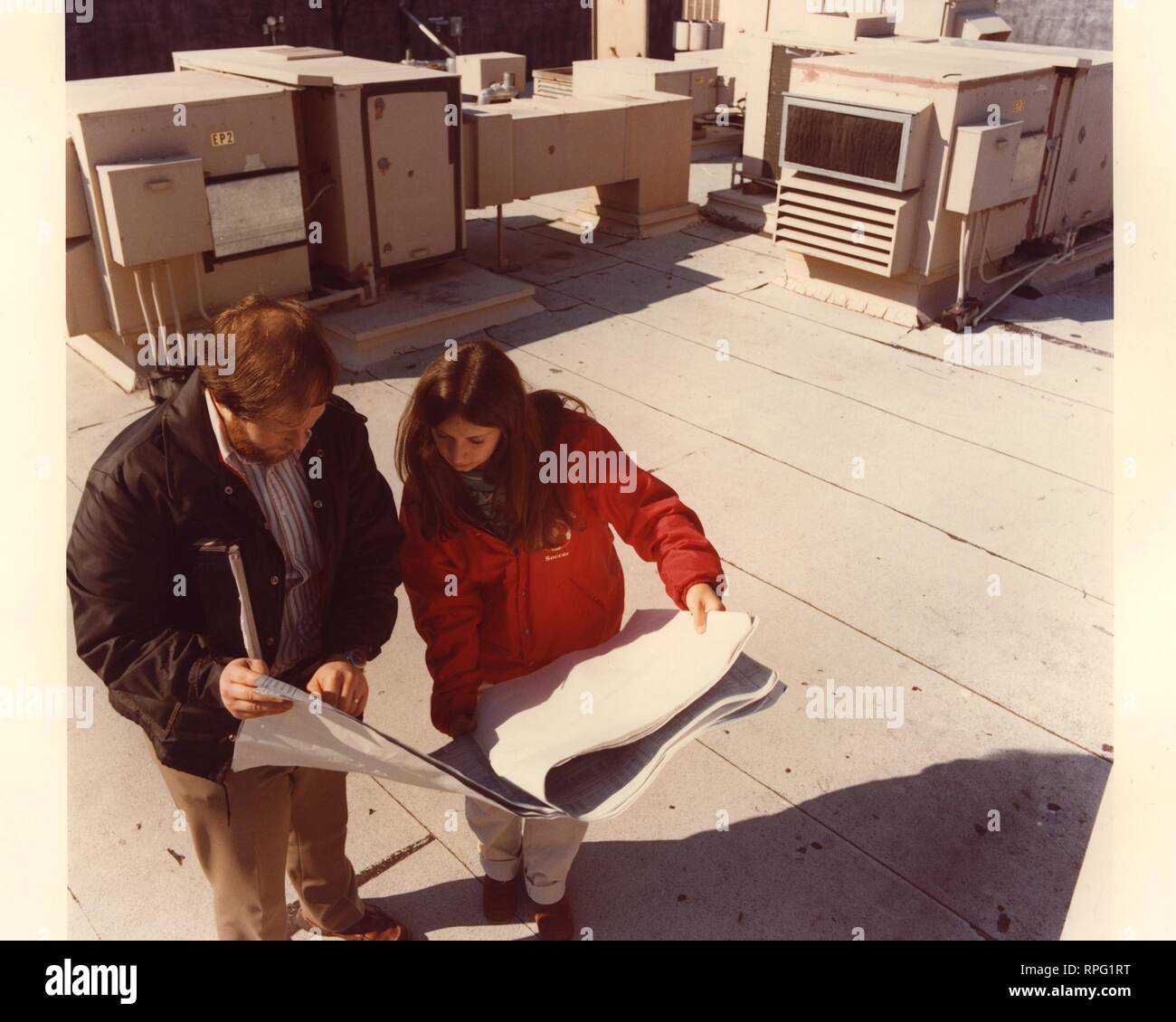 Elevato angolo di visione di un uomo e di una donna in piedi su un tetto, l'esame di una serie di piani di ingegneria a Oak Ridge National Laboratory, Oak Ridge, Tennessee, 1990. Immagine cortesia del Dipartimento Americano di Energia. () Foto Stock