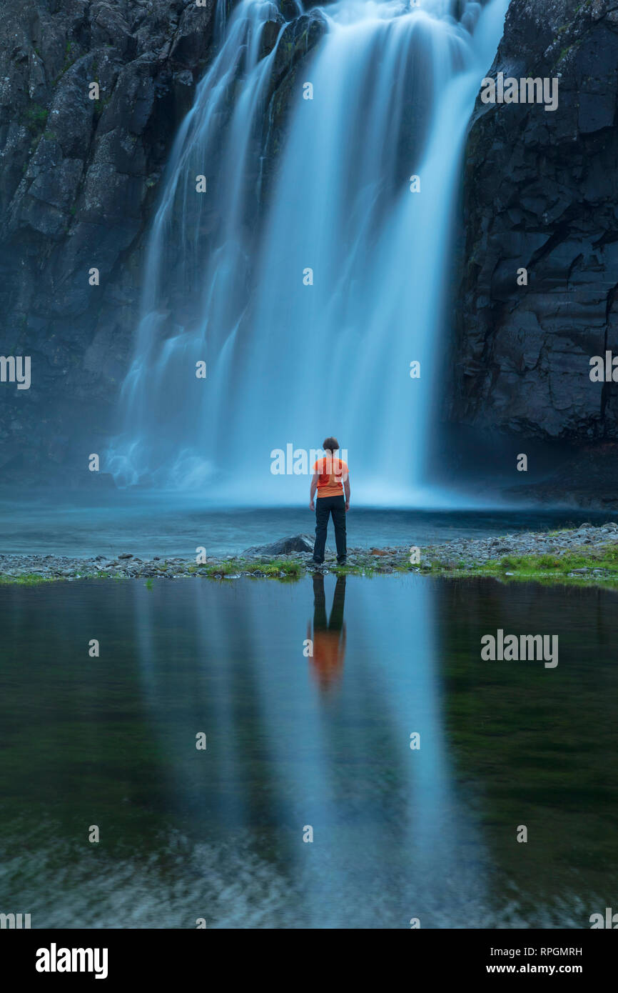 Persona riflessa sotto Foss cascata, sulla riva di Fossfjordur. Westfjords, Islanda. Foto Stock