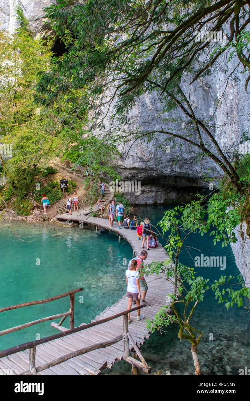 I turisti passeggiare lungo la passerella di legno che attraversa il flusso di acqua verso una serie di gradini di pietra a Plivice Lakes National Park, Croazia Foto Stock