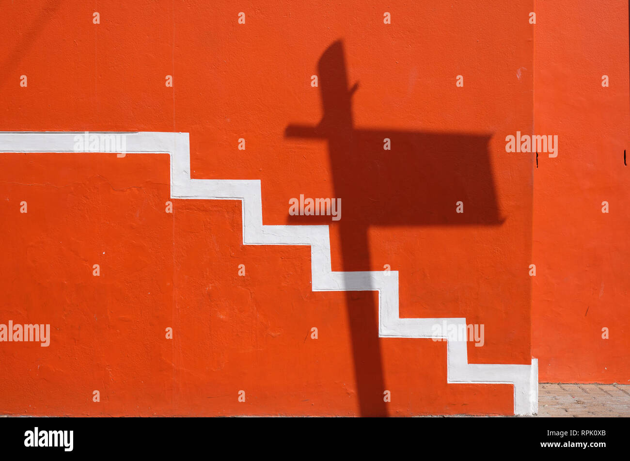 Dettagli da le variopinte facciate delle case a Bo Kaap, minimale che mostra di bianco stair progressione su parete arancione, con ombre di un cartello stradale Foto Stock