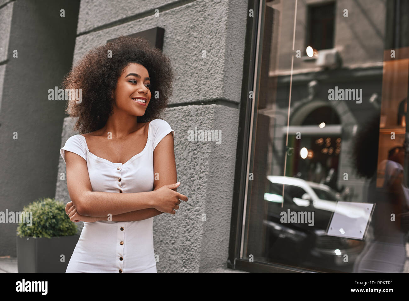 Giovane e piena di energia. Ritratto della splendida Afro American woman standing all aperto con bracci incrociati e sorridente. Aspetto di moda Foto Stock