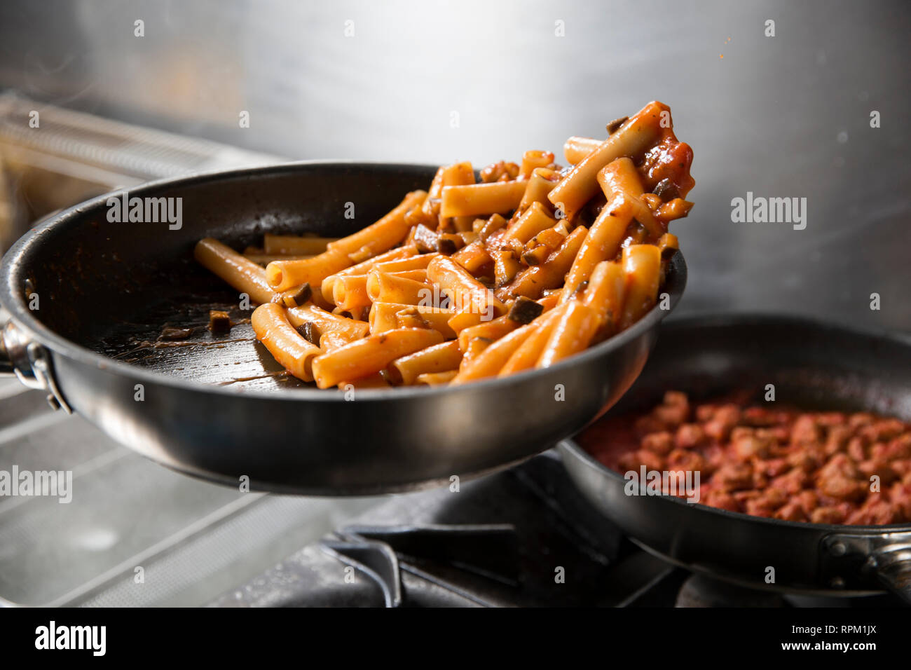 Primo piano di uno chef professionale la cottura di deliziosi piatti di pasta in una padella la fase finale prima di servire il suo piatto. Foto Stock