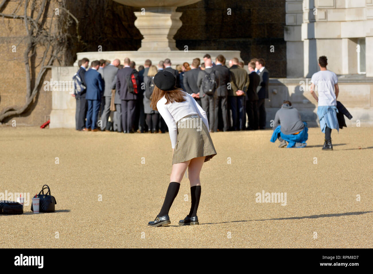 Londra, Inghilterra, Regno Unito. Giovane donna che posa per una foto alla Horse Guards Parade in una calda giornata di sole a febbraio 2019. Gruppo di uomini sullo sfondo Foto Stock