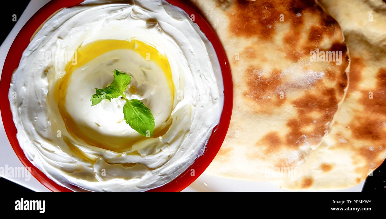 Vista superiore della labneh e pita pane piatto, con le foglie di menta e olio di oliva. Arab salsa di yogurt, spessa e crema spalmabile. Foto Stock
