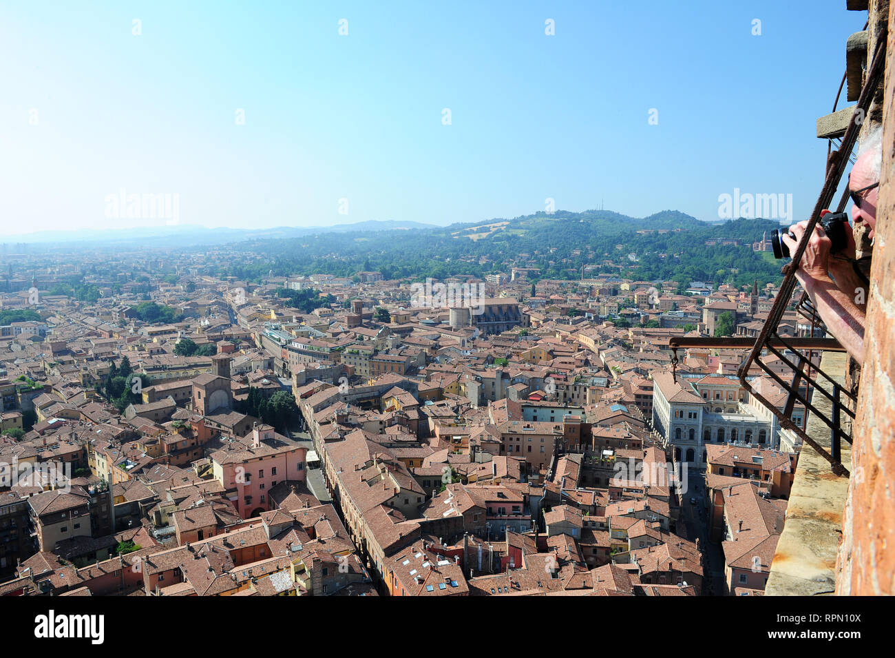 Un uomo appoggiato su di una finestra sulla sommità della torre degli Asinelli a Bologna per scattare una foto della città al di sotto di Foto Stock