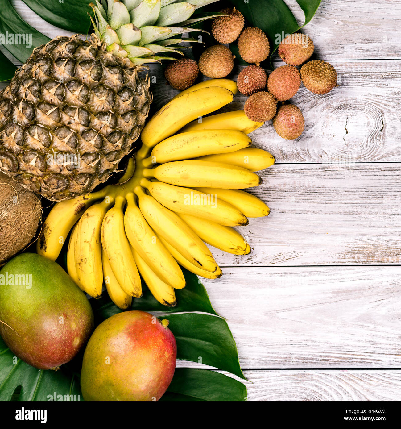 Frutta fresca tropicale su legno vista dall'alto. banane, ananas, noce di cocco, mango, litchi castagne Foto Stock