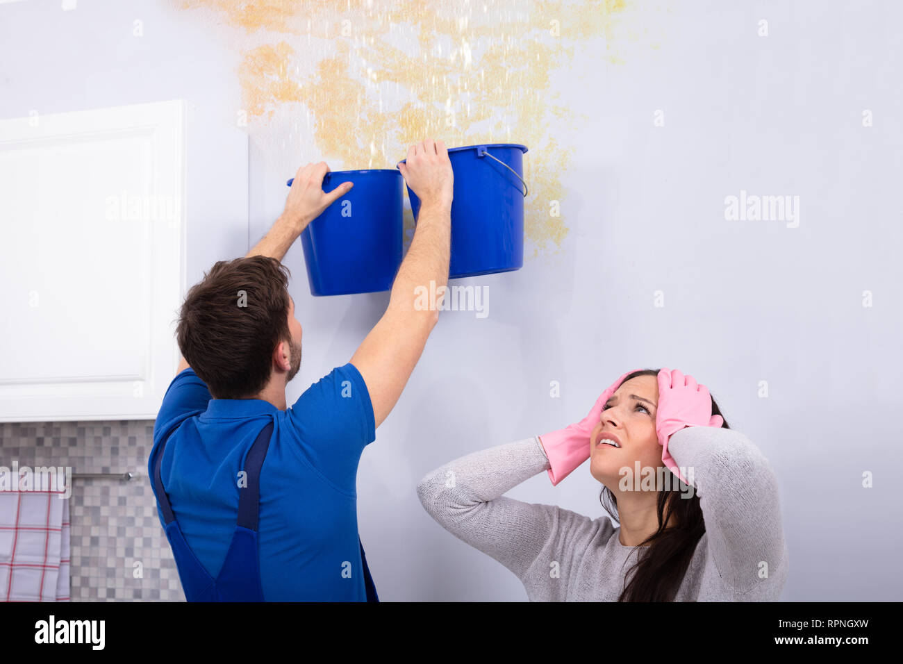 Frustrare la donna con tuttofare raccolta di acqua dal soffitto danneggiato in blu la benna Foto Stock