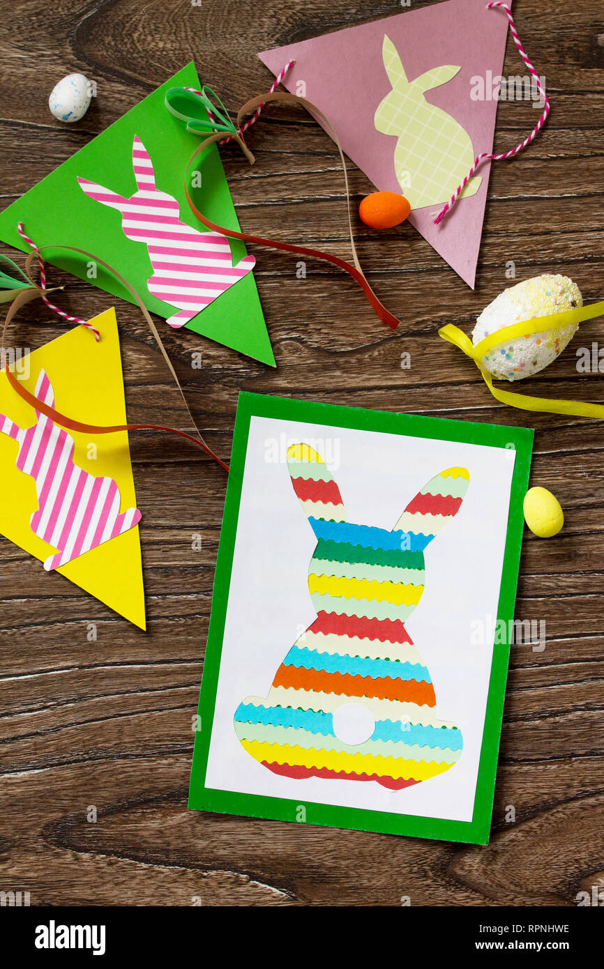 Cartolina di pasqua coniglietto di Pasqua e la pasqua i bambini garland su un tavolo di legno. Fatte a mano. Progetto di la creatività dei bambini, artigianato e mestieri per i bambini. Foto Stock