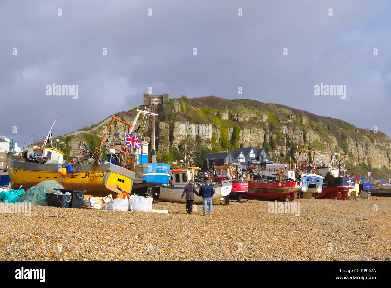 Giovane passeggiando passato Hastings barche da pesca sulla Città Vecchia Stade spiaggia un giorno di tempesta in inverno, East Sussex, Regno Unito Foto Stock