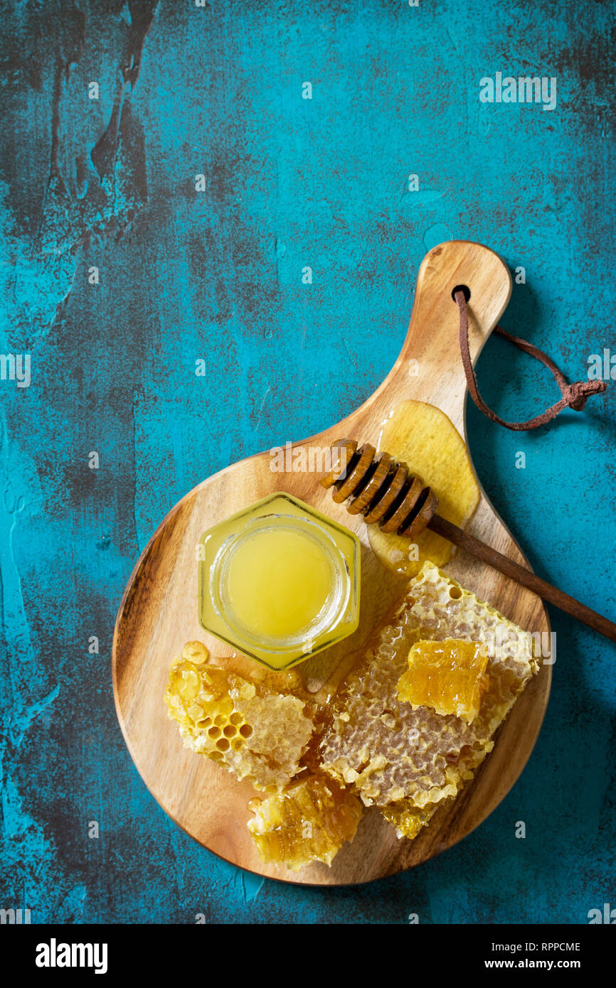 Miele naturale. Il miele nel vasetto di vetro e bilanciere, dolce favi su pietra blu nella tabella. Vista superiore piatta sullo sfondo dei laici. Copia dello spazio. Foto Stock