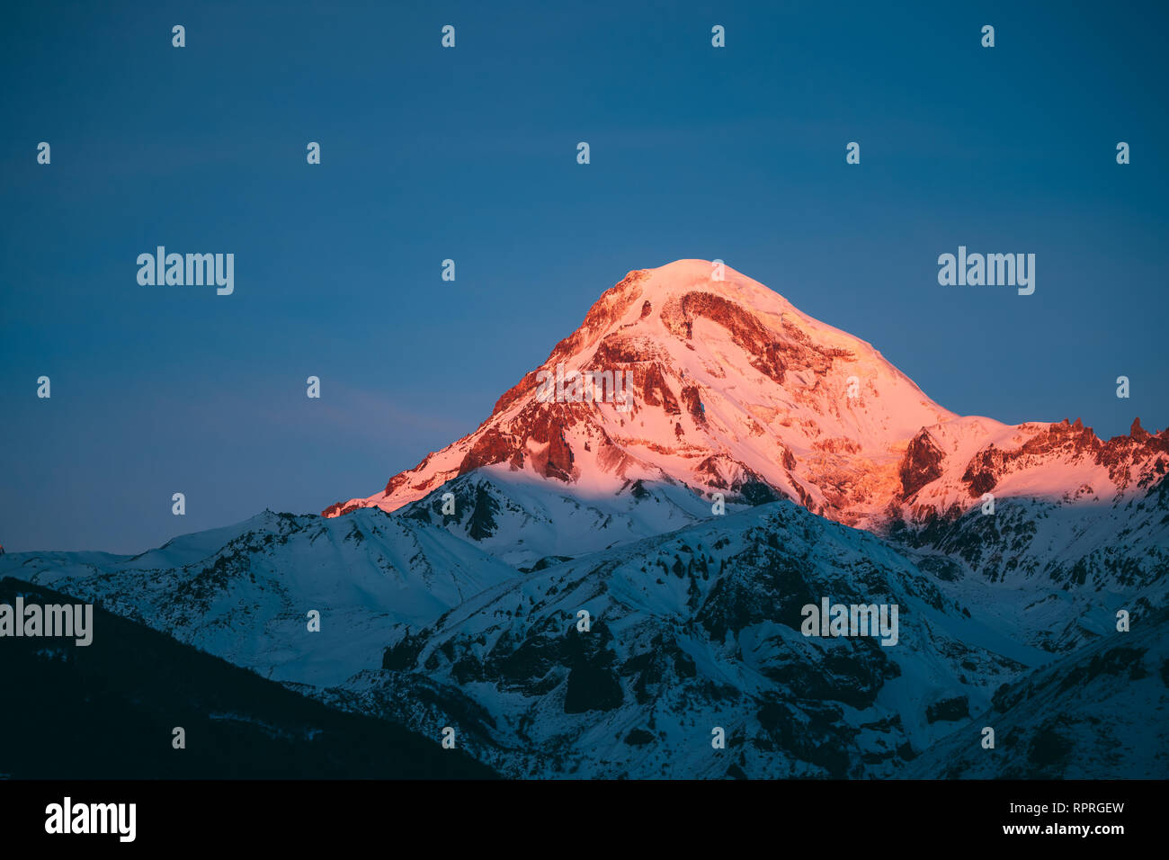 La Georgia. Mount Kazbek coperte di neve in inverno Sunrise. Mattina Alba sommità colorata di montagna in rosa-arancio. Awesome inverno natura georgiano Foto Stock