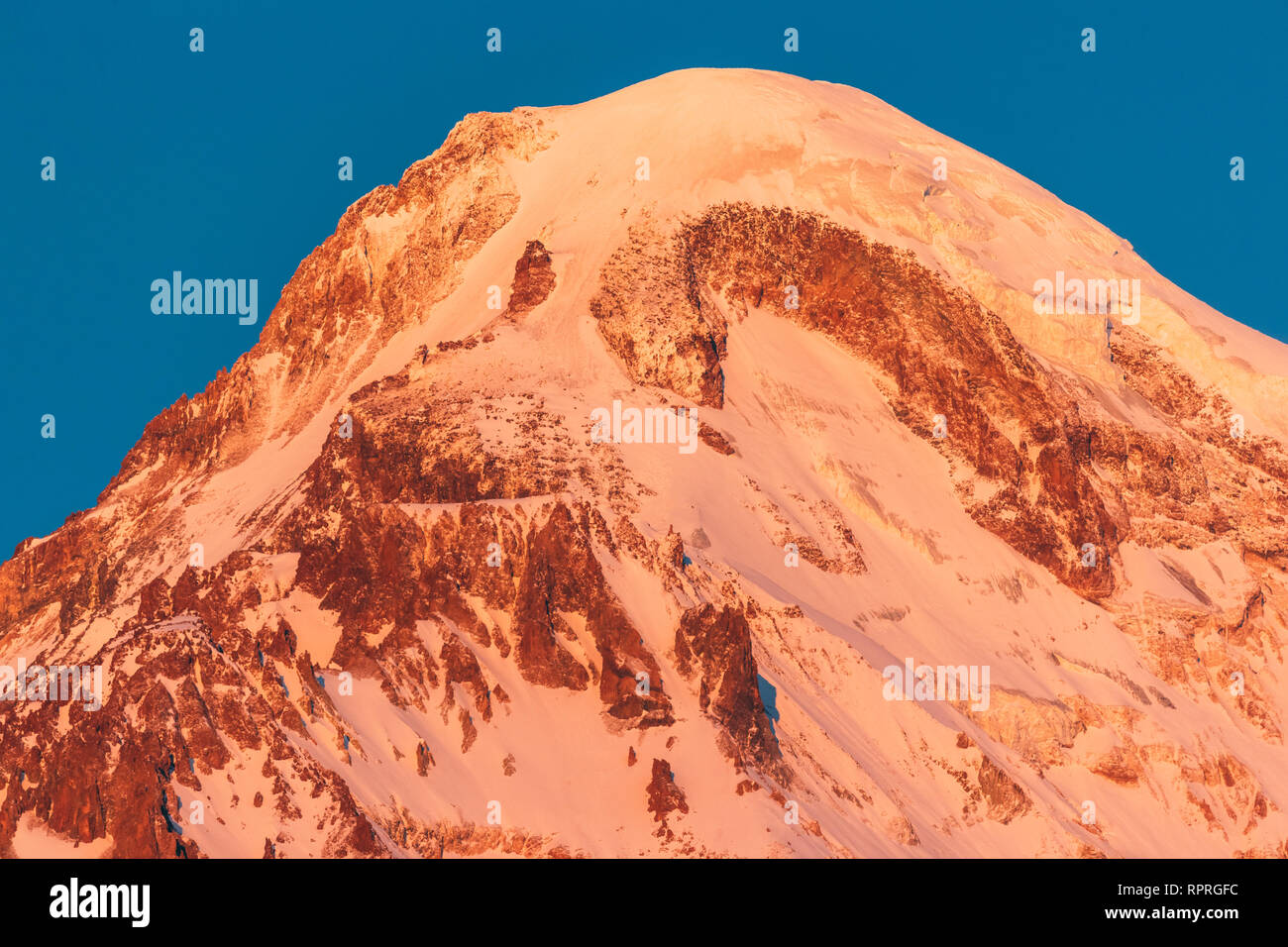 La Georgia. Mount Kazbek coperte di neve in inverno Sunrise. Mattina Alba sommità colorata di montagna in rosa-arancio. Awesome inverno natura georgiano Foto Stock