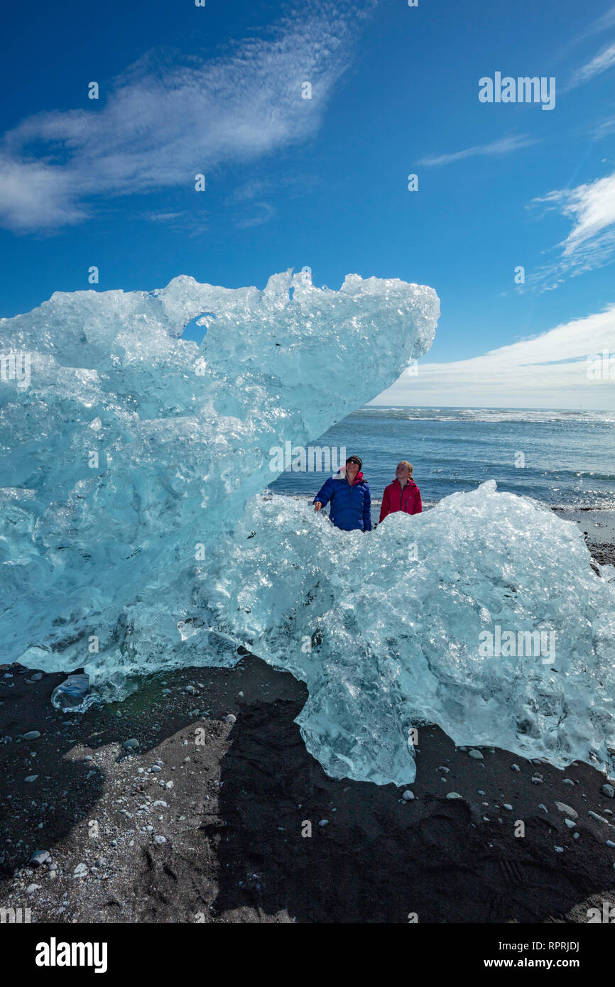 Persone esaminando iceberg Breidamerkursandur sulla spiaggia di sabbia nera, al di sotto di Jokulsarlon. Sudhurland, sud est dell'Islanda. Foto Stock