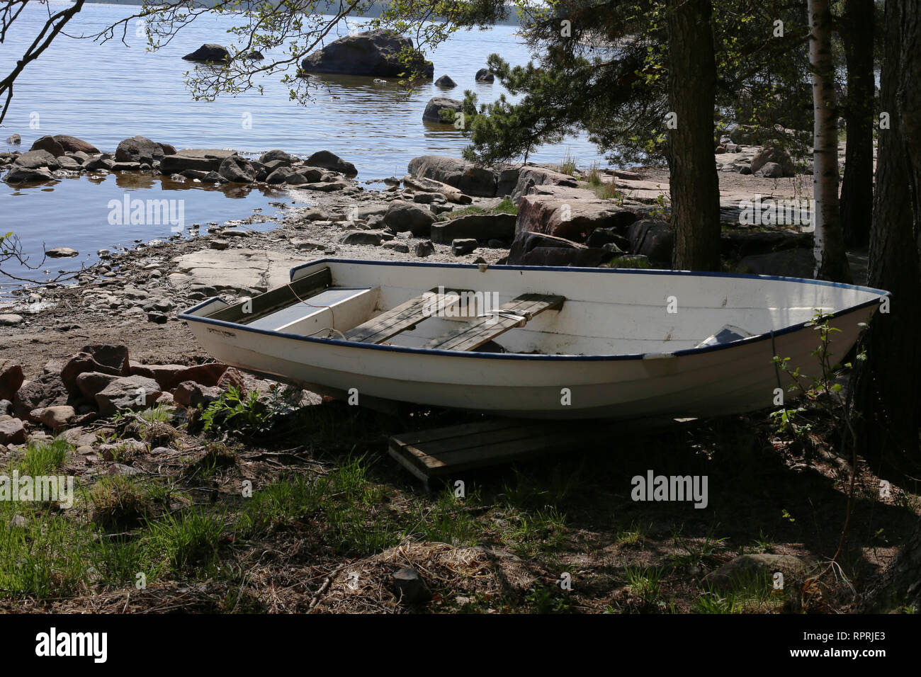 La barca di legno sulla costa. Vi è una certa quantità di acqua, roccia, erba e alberi nella foto in aggiunta alla barca a remi. Fotografato durante l estate in Finlandia. Foto Stock