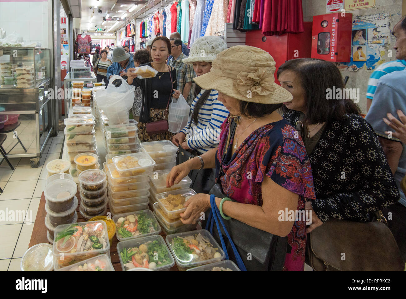 Le donne si affollano attorno a un tavolo impilati con plastica i contenitori da asporto di pre-cottura pasti presso un negozio di Cabramatta a Sydney in Australia Foto Stock