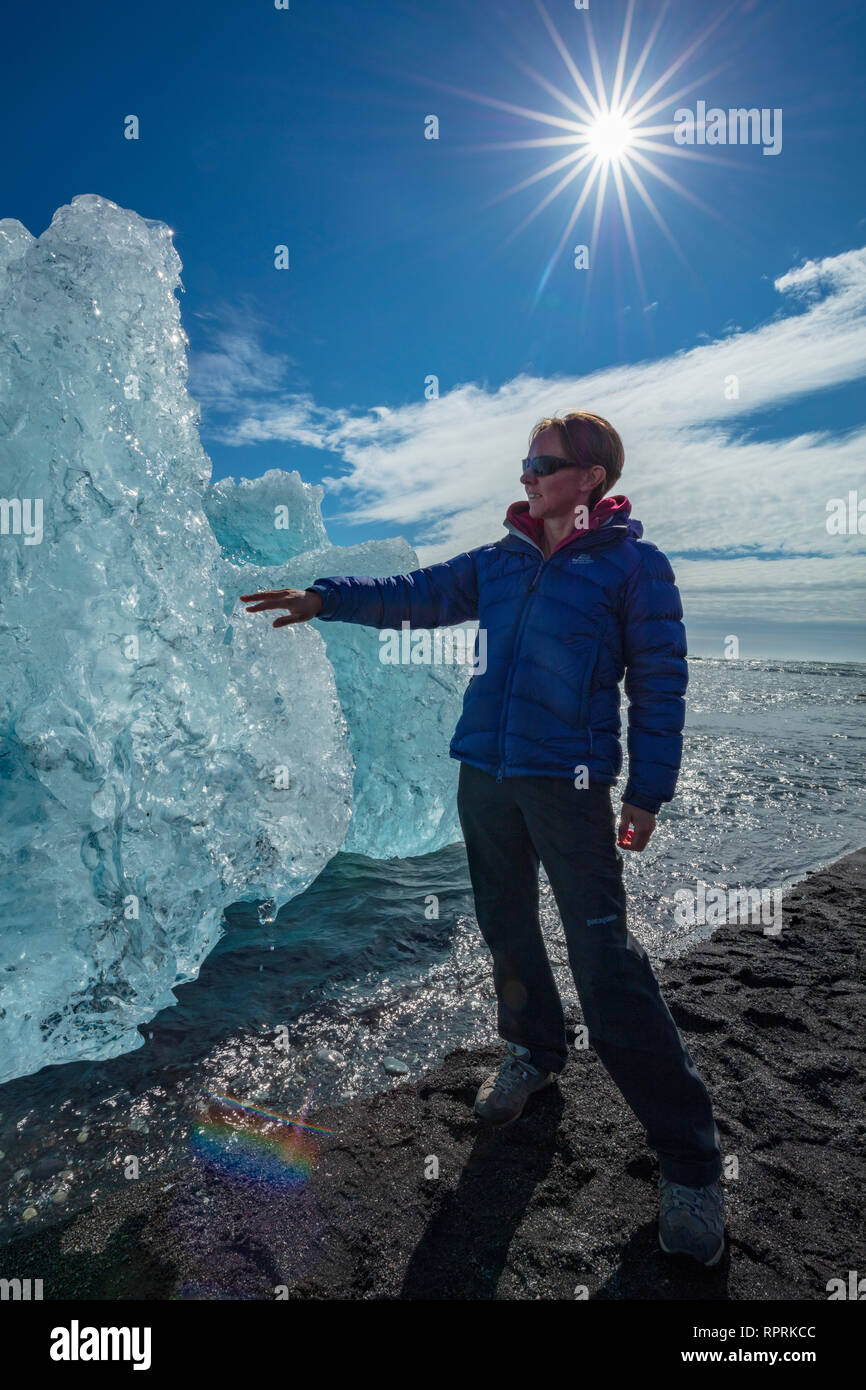 Persona esaminando un iceberg Breidamerkursandur sulla spiaggia di sabbia nera, al di sotto di Jokulsarlon. Sudhurland, sud est dell'Islanda. Foto Stock