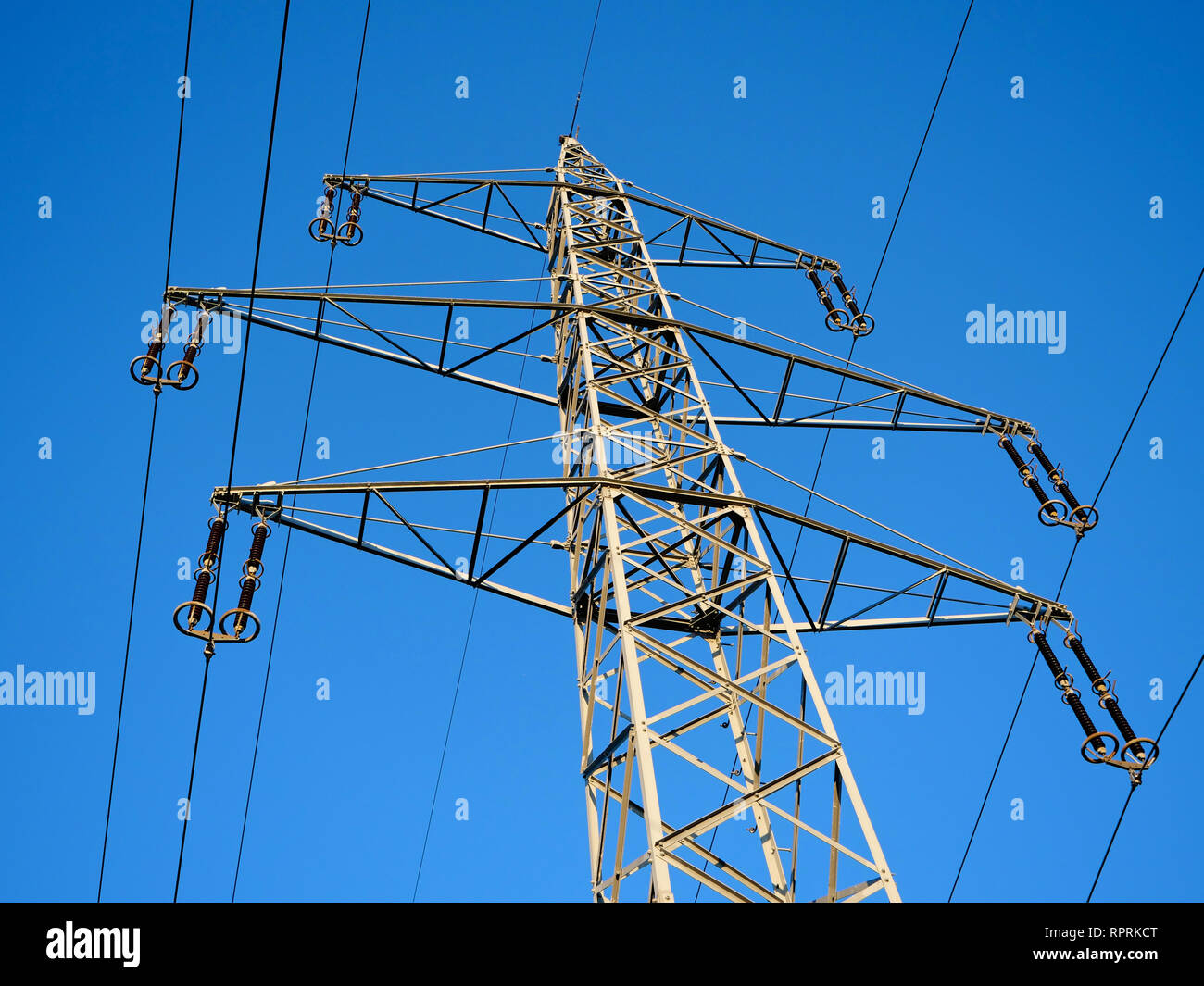 Un valore di tensione alto traliccio di potenza contro un luminoso cielo blu in campagna Foto Stock