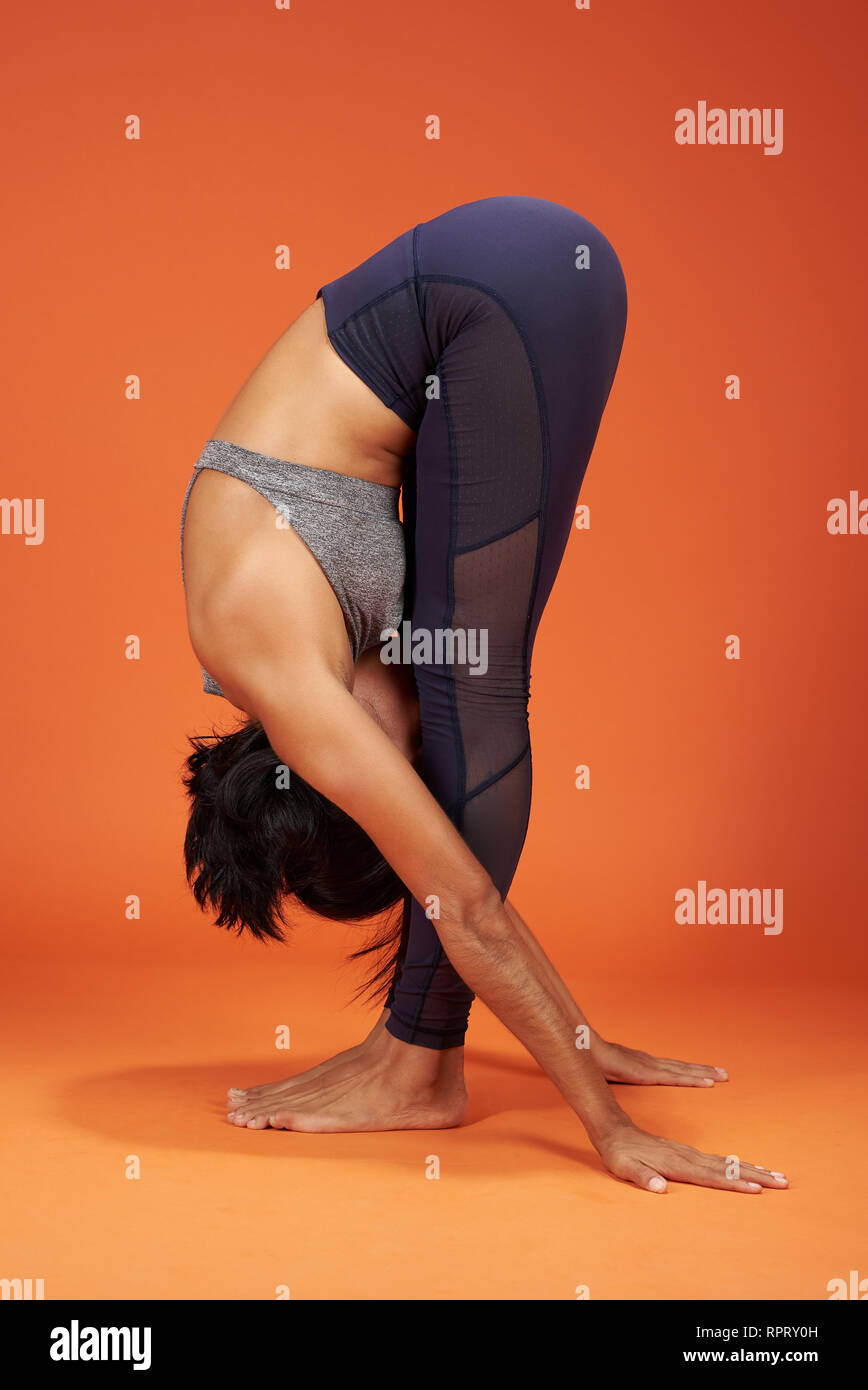 Permanente di piegare in avanti lo Yoga asana che mostra una donna su orange il colore di sfondo per studio Foto Stock