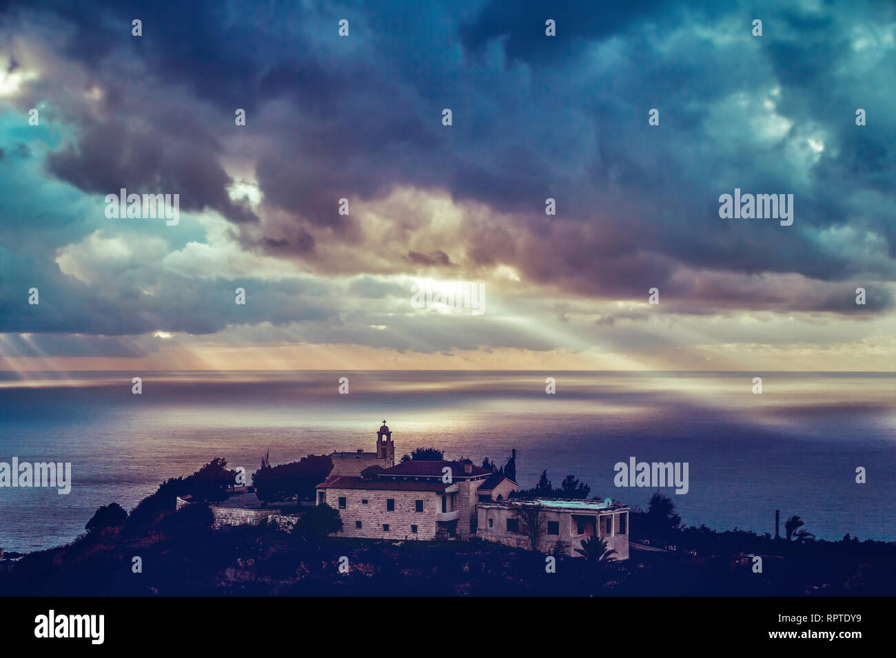 Bellissima vista su una chiesa costiera nel buio di sera Nuvoloso, i raggi del sole che si infrangono sulla l'acqua attraverso le nuvole come se la voce di Dio Foto Stock