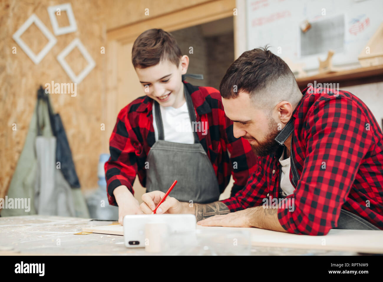 Focalizzato artigiano e il suo piccolo ragazzo di inseguitore di misurazione di legno utilizzando un righello e matita in officina. Uomo adulto confronta il corretto markup in wo Foto Stock