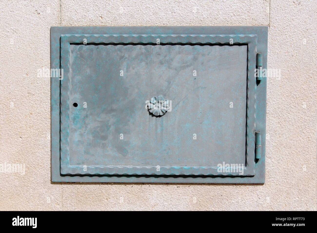 Pesante ferro il coperchio con il bordo decorativo montato su telaio metallico con le cerniere sul muro di casa con la nuova facciata sulla calda giornata di sole Foto Stock
