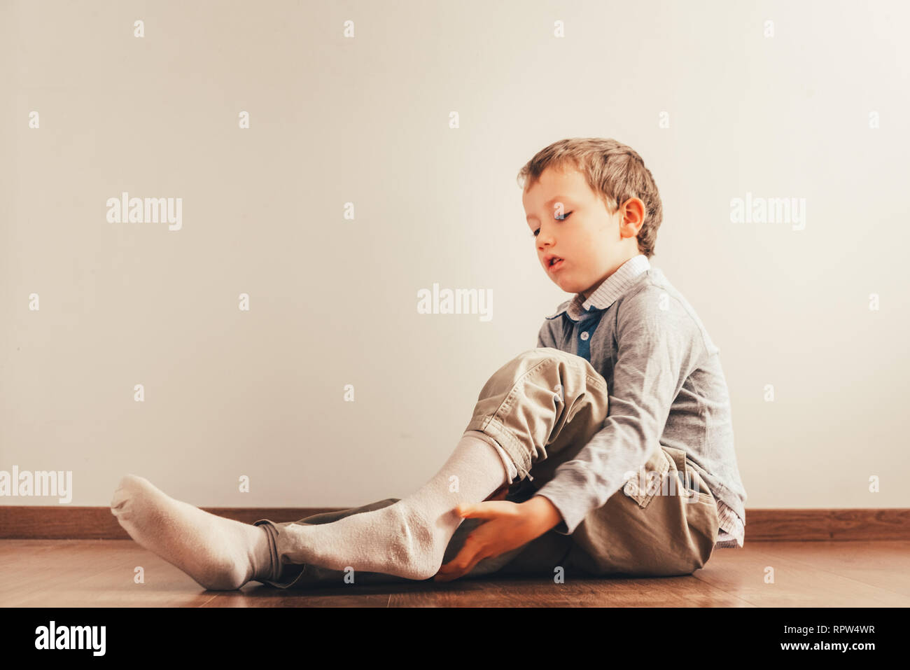 Bambino con un sacco di indipendenza seduta sul pavimento mettendo sul suo calze  con un espressione di sforzo Foto stock - Alamy