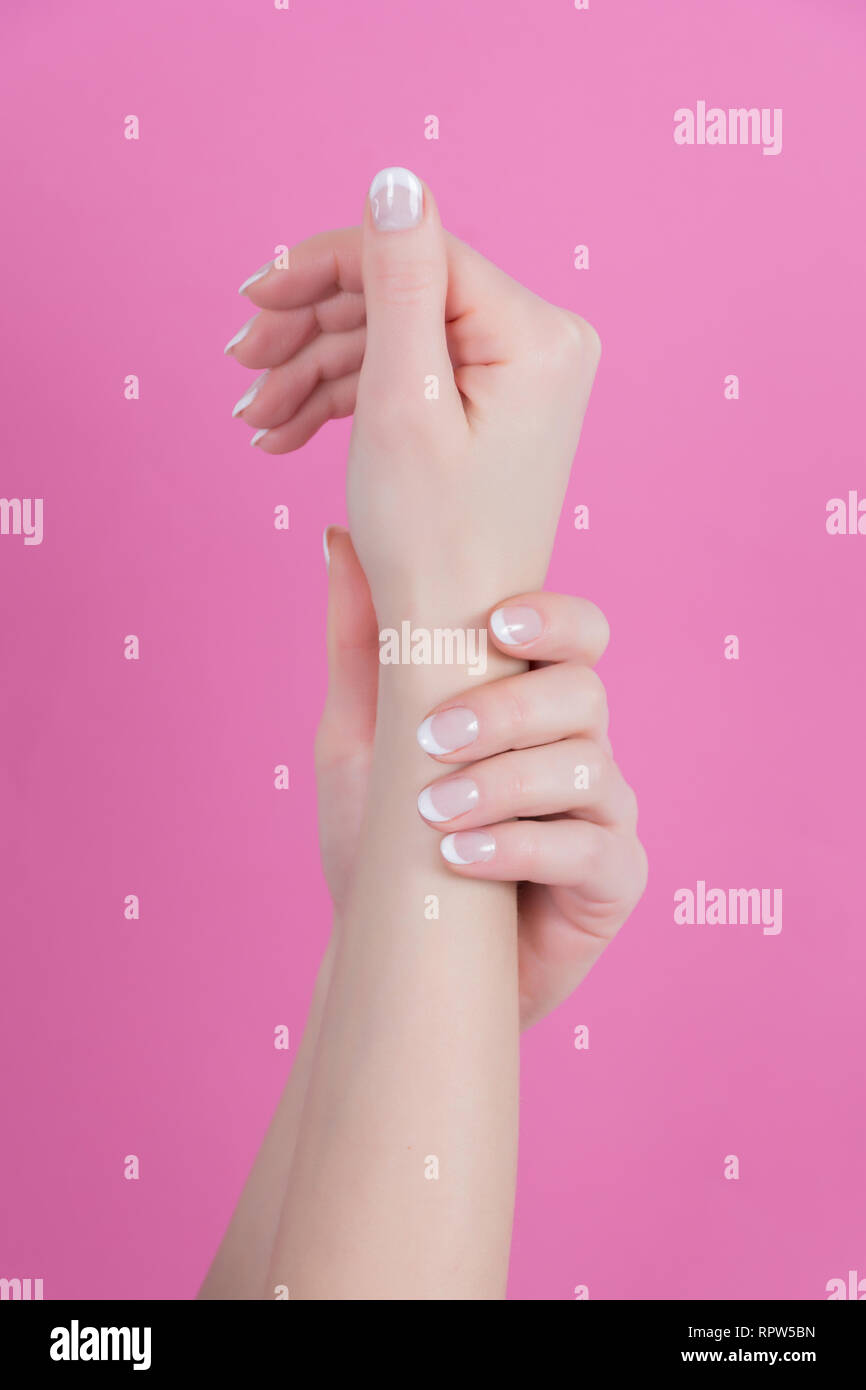Giovane donna mani con Unghie french manicure style isolati su sfondo rosa in studio. Bellezza e chiodi concetto polacca. Close up, il fuoco selettivo Foto Stock