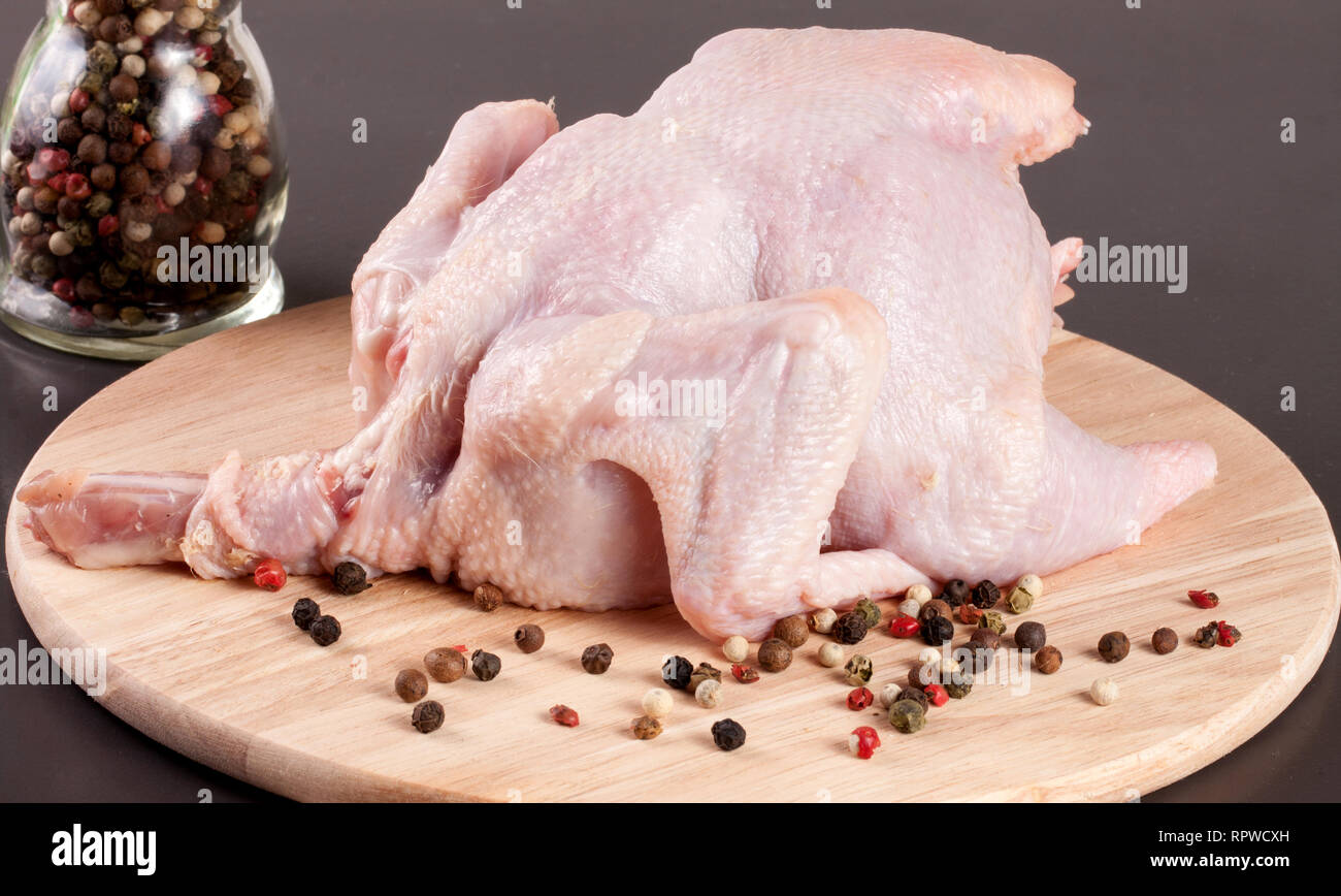Il pollo crudo carcassa con chicchi di pepe nero su sfondo scuro Foto Stock