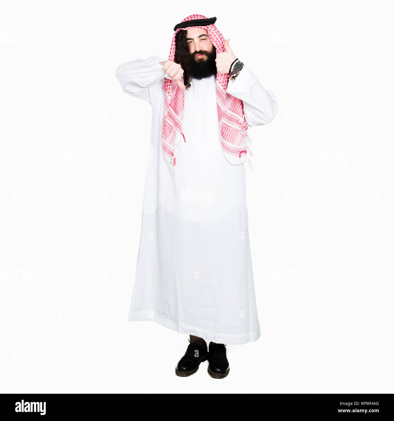 Arabian business man con capelli lunghi indossando il tradizionale keffiyeh sciarpa facendo pollice in su e in giù, disaccordo e accordo di espressione. Crazy conflitto Foto Stock